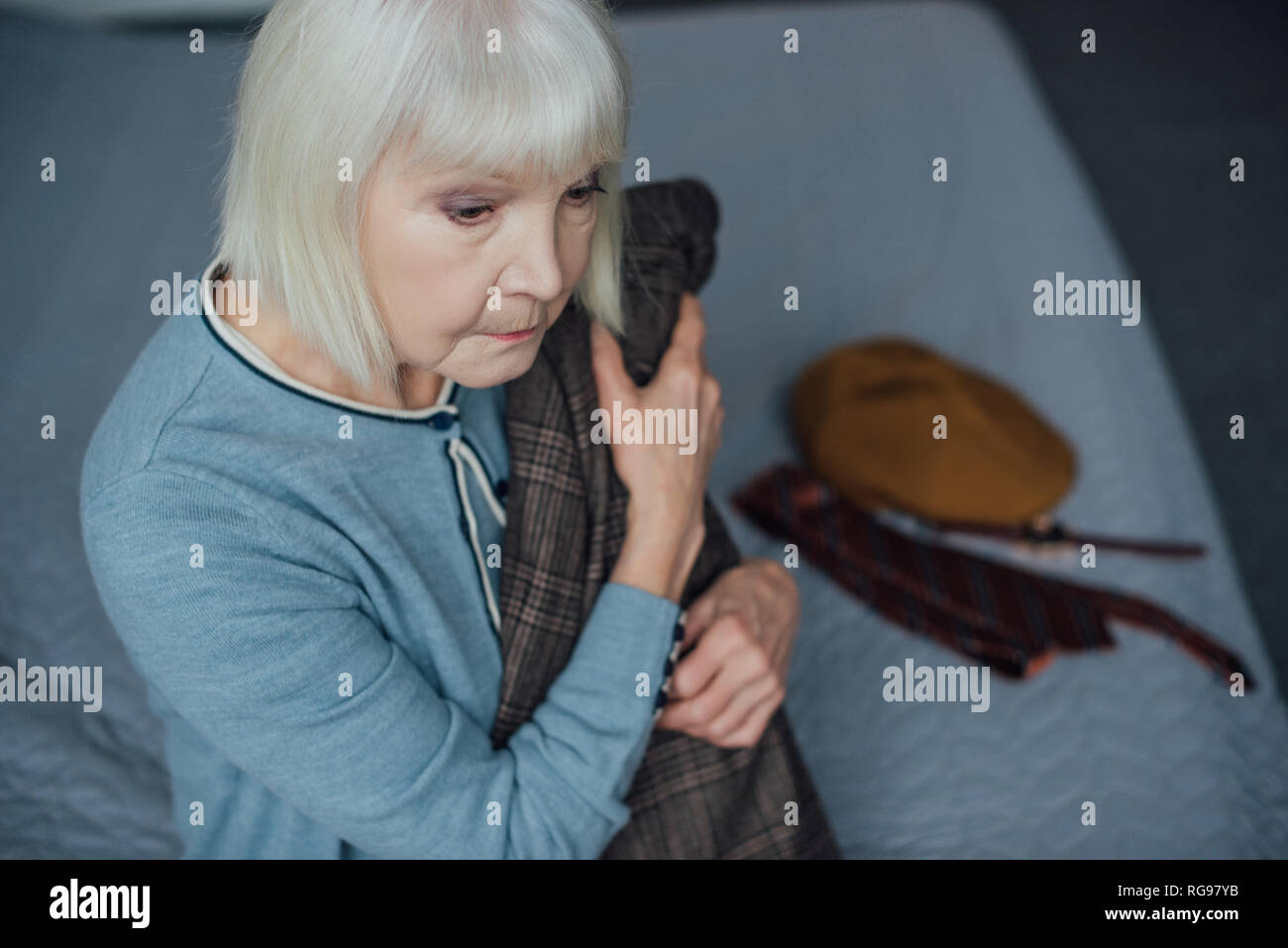 Contrarié senior woman aux cheveux gris assis sur le lit et la tenue de la gaine à Accueil Banque D'Images