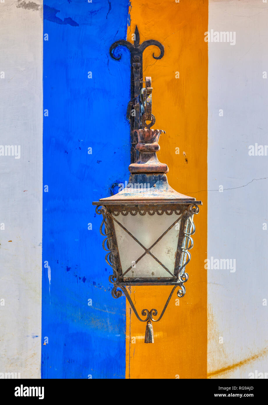 Photographie d'une vieille lampe fer forgé streep contre un jean bleu et jaune mur de plâtre pris dans le village médiéval d'Obidos, Portugal. Banque D'Images
