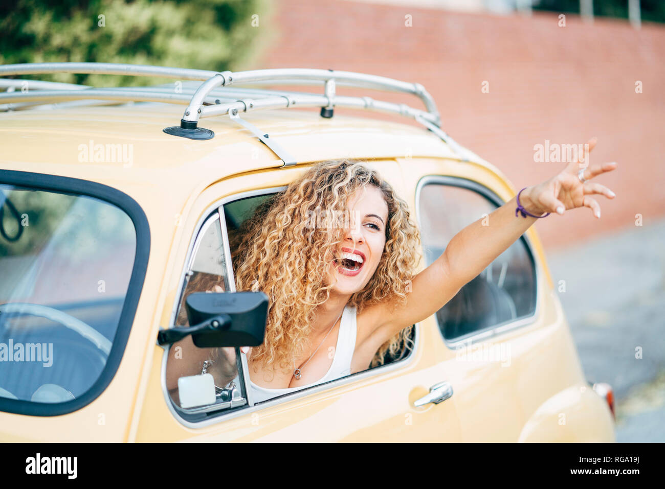 Portrait of happy blonde woman leaning out de la fenêtre de voiture classique montrant la victoire Banque D'Images