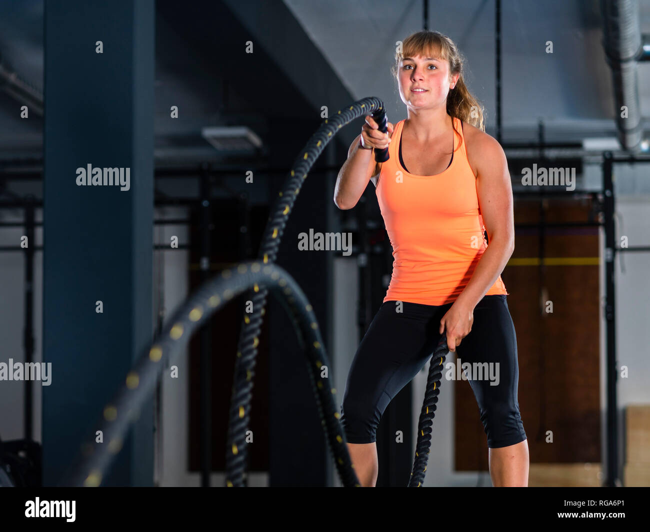 Athletic young woman exercising with ropes bataille at gym Banque D'Images