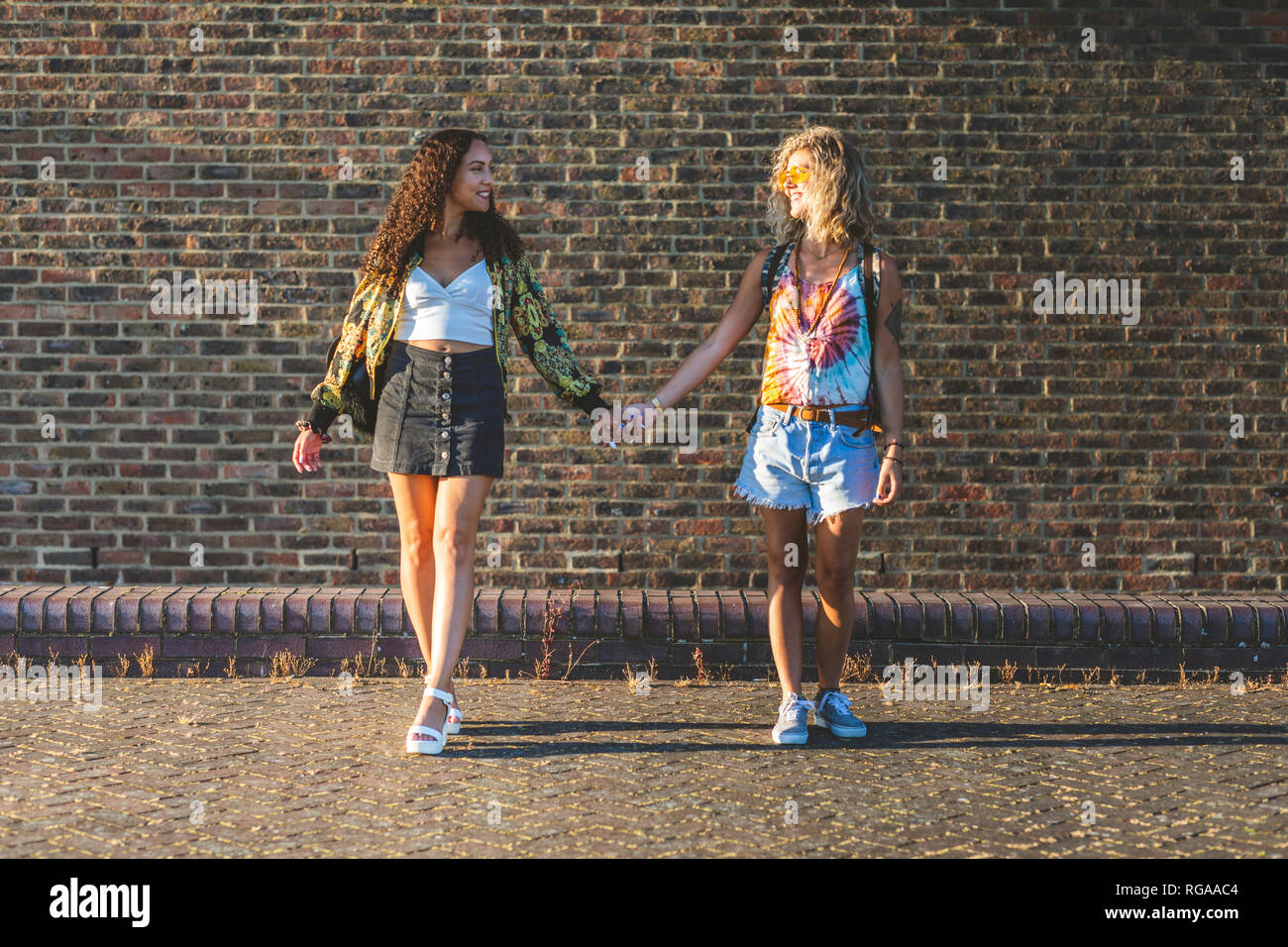 Deux jeunes femmes se tenant la main en face de mur de brique Banque D'Images
