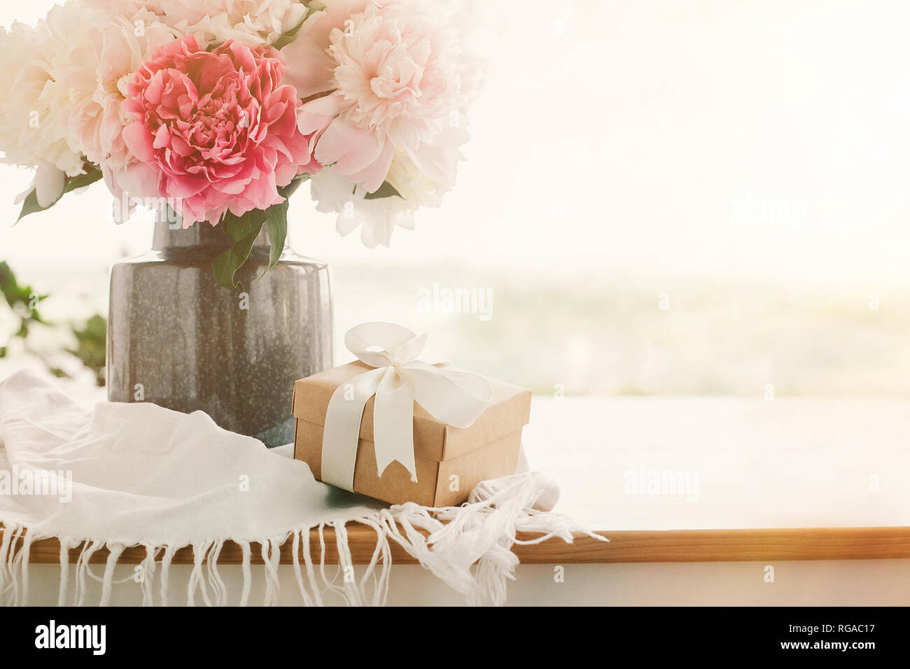 Heureuse fête des mères, carte de souhaits. Belles pivoines dans un vase et  boîte-cadeau sur une table en bois rustique dans la lumière du matin  ensoleillé avec de l'espace pour le texte.