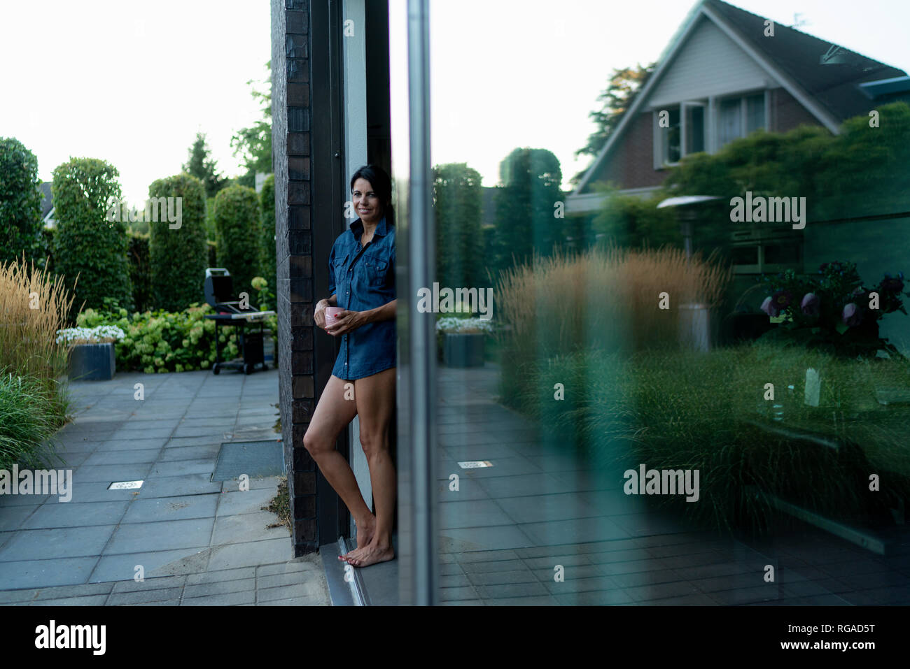 Femme debout sur une terrasse d'une maison moderne tenant une chope Banque D'Images Femme debout sur une terrasse d'une maison moderne tenant une chope Banque D'Images