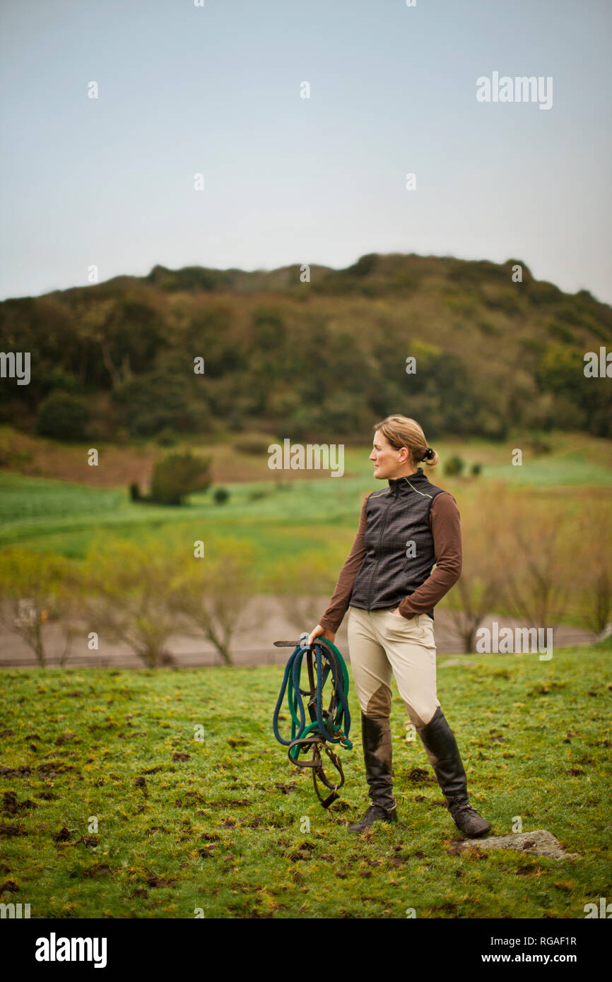 Mid adult woman se préparer à aller de l'équitation dans un pâturage. Banque D'Images