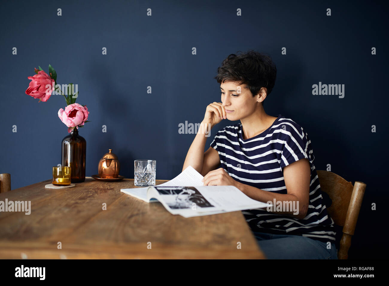 Femme à la maison assis à table en bois la lecture d'un magazine Banque D'Images