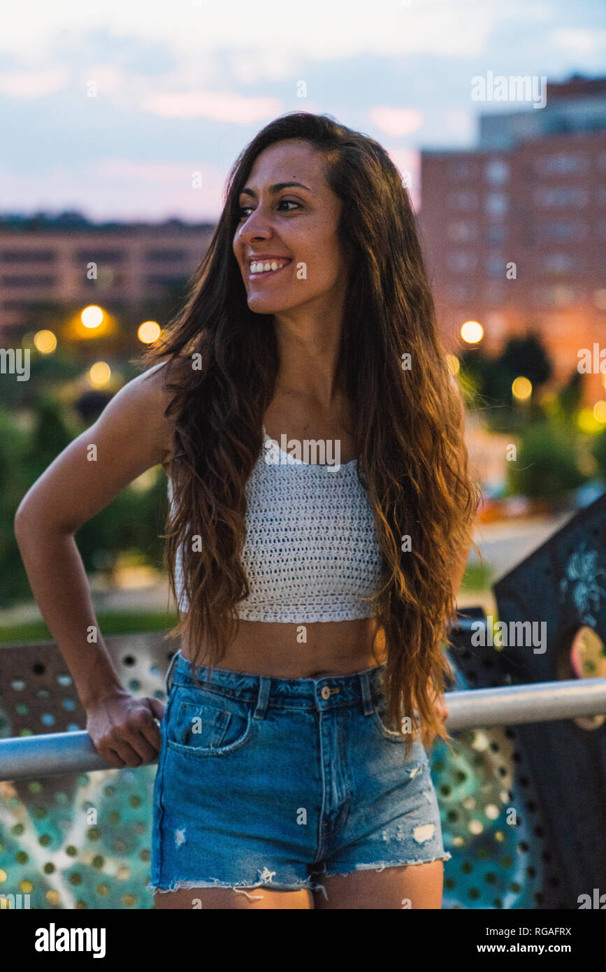 Belle jeune femme avec de longs cheveux bruns dans la ville au crépuscule Banque D'Images
