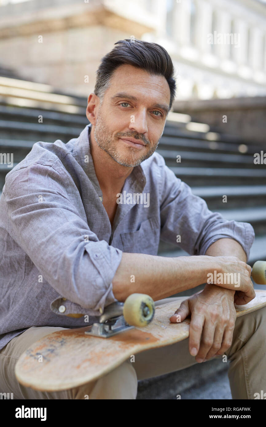 Portrait de relaxed mature man with skateboard assis sur des escaliers Banque D'Images