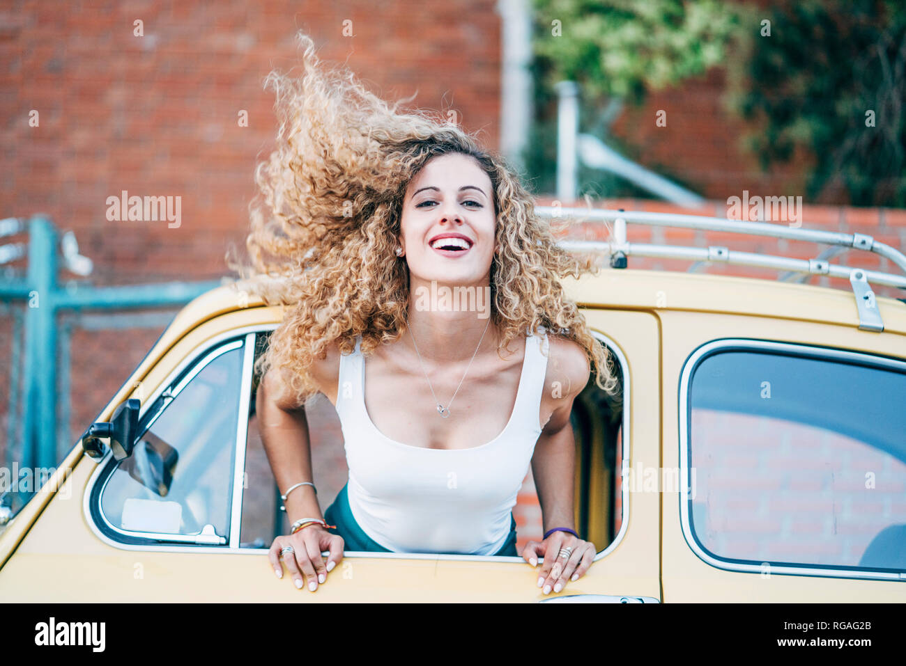 Portrait de femme blonde incliné vers l'extérieur de la fenêtre de voiture classique rejetant ses cheveux Banque D'Images
