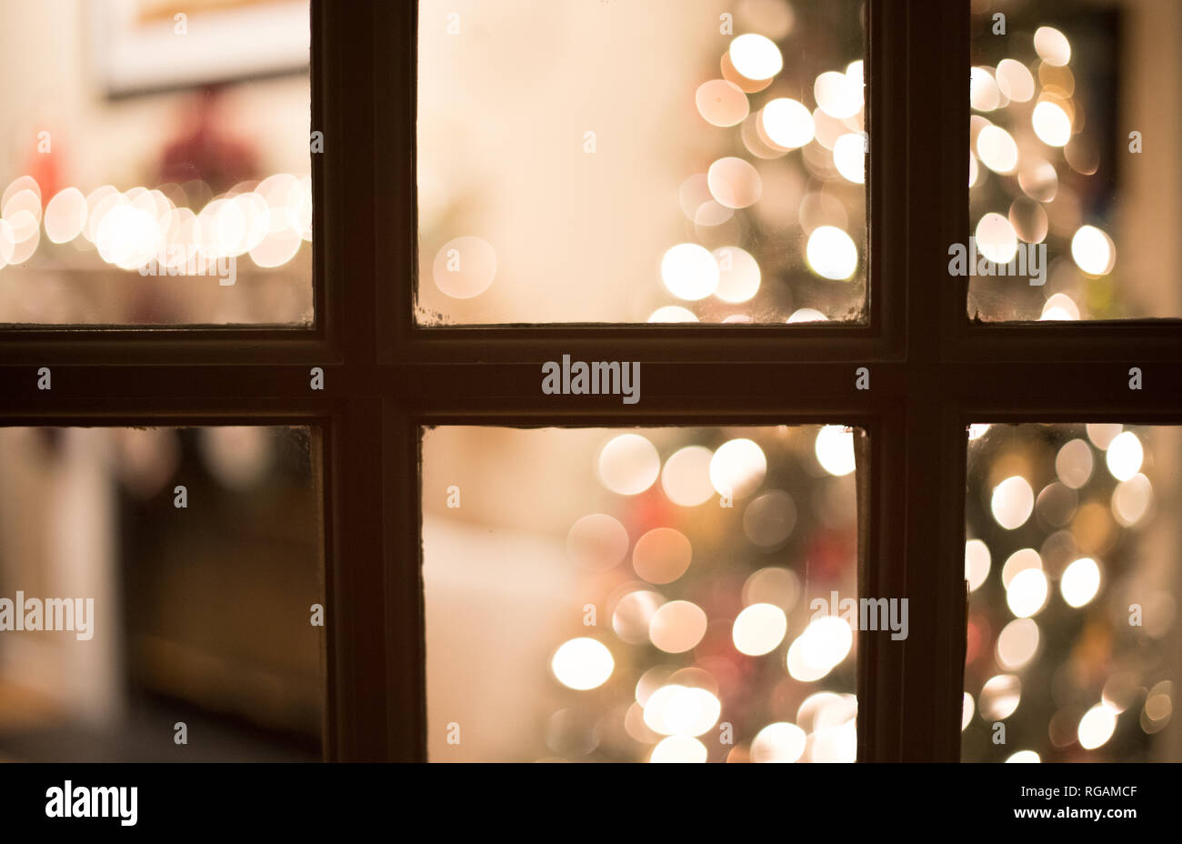 Flou d'une photo à travers une fenêtre, la nuit dans un salon décoré pour Noël. Banque D'Images