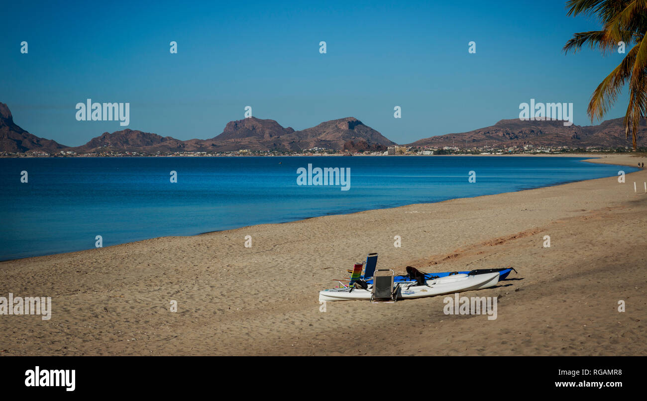 Les kayaks et les chaises de plage sur une plage de sable fin avec la ville de San Carlos dans la distance. Péninsule de Bahia, la côte du Pacifique, Mexique Banque D'Images