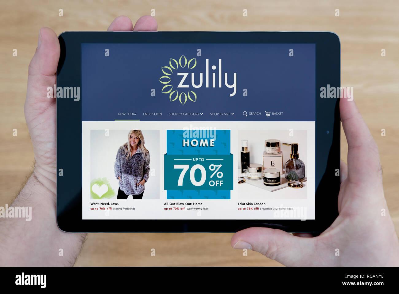 Un homme regarde la Zulily site sur son iPad tablet device, tourné contre une table en bois page contexte (usage éditorial uniquement) Banque D'Images