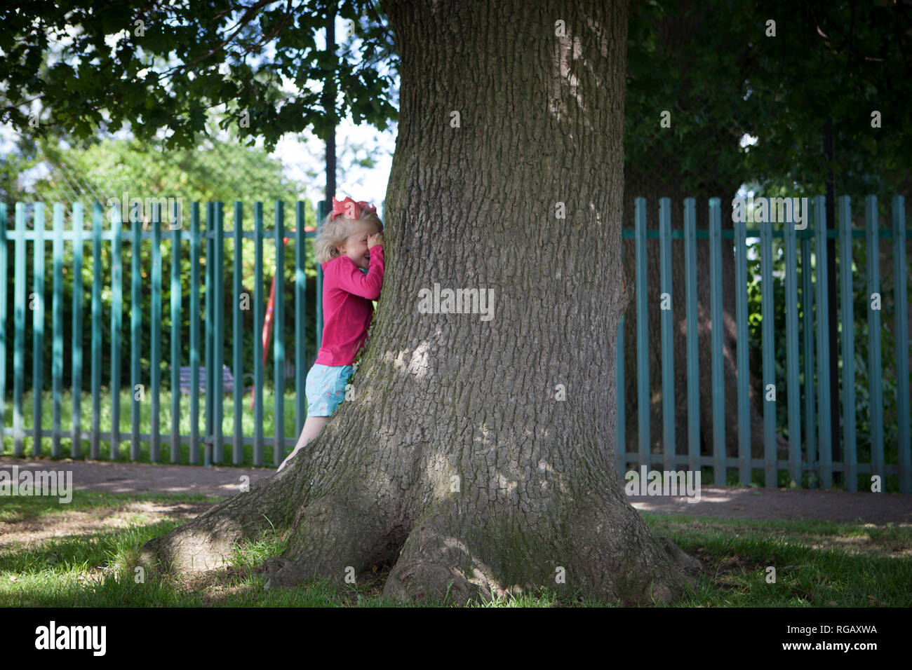 Jeune fille de race blanche oeil derrière un arbre et de rire Banque D'Images