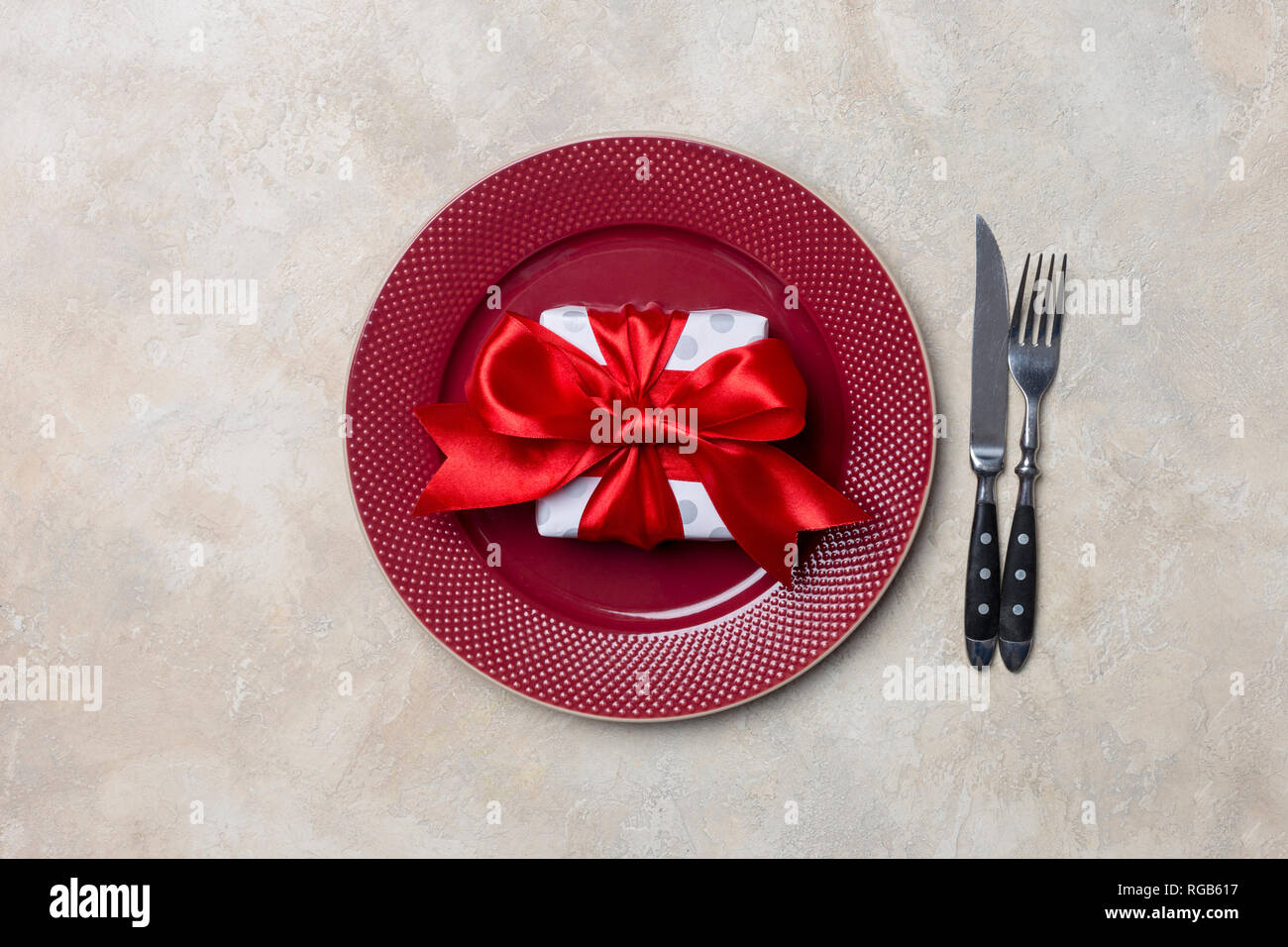 Plaque rouge avec boîte-cadeau avec ruban rouge, près de fourchette et couteau, à fond blanc Banque D'Images Plaque rouge avec boîte-cadeau avec ruban rouge, près de fourchette et couteau, à fond blanc Banque D'Images