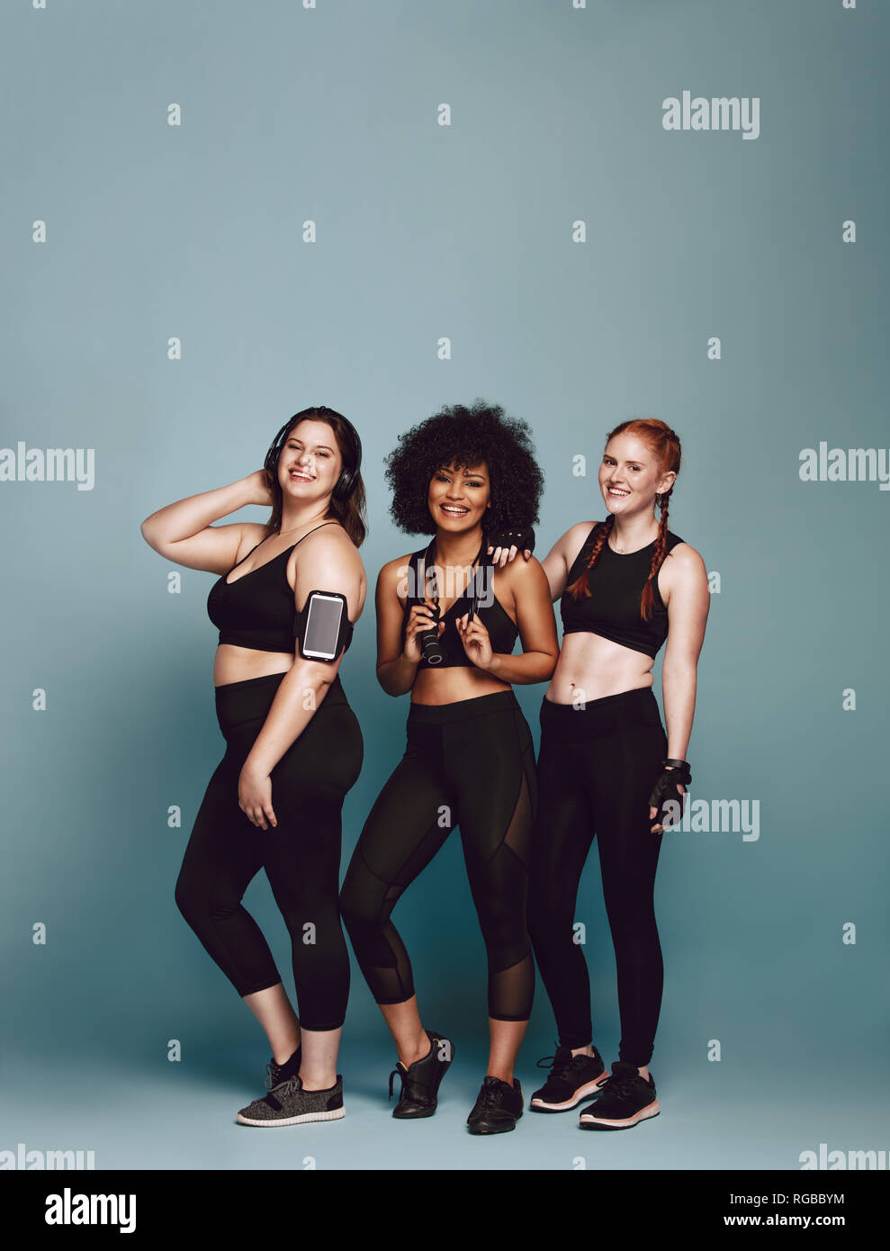 Groupe des femmes dans divers sportswear Standing together sur fond gris. Trois femmes de différents poids dans l'habillement de remise en forme. Banque D'Images