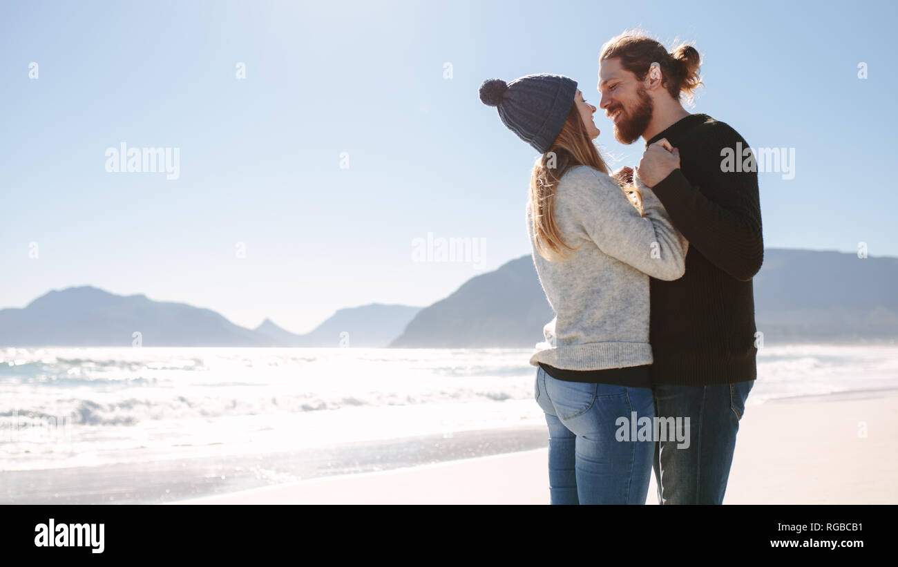 Couple romantique au bord de la mer. L'homme et la femme debout près de l'autre sur la plage à la recherche à l'autre tenant la main et sourit. Banque D'Images