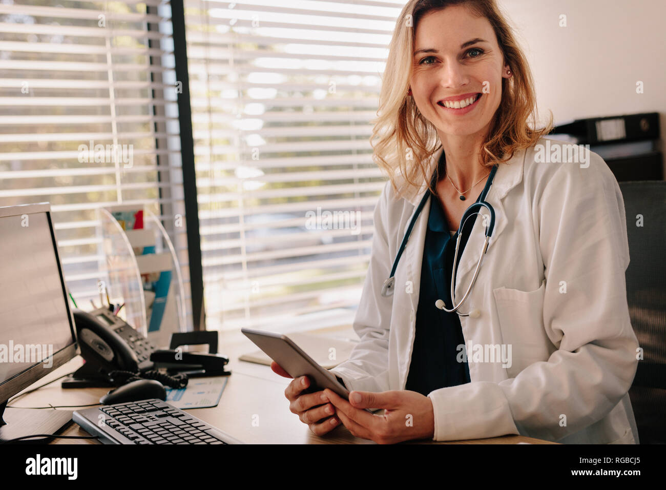 Médecin femme assise à son bureau avec une tablette numérique. Femme médecin positive looking at camera avec sourire sur le visage. Banque D'Images