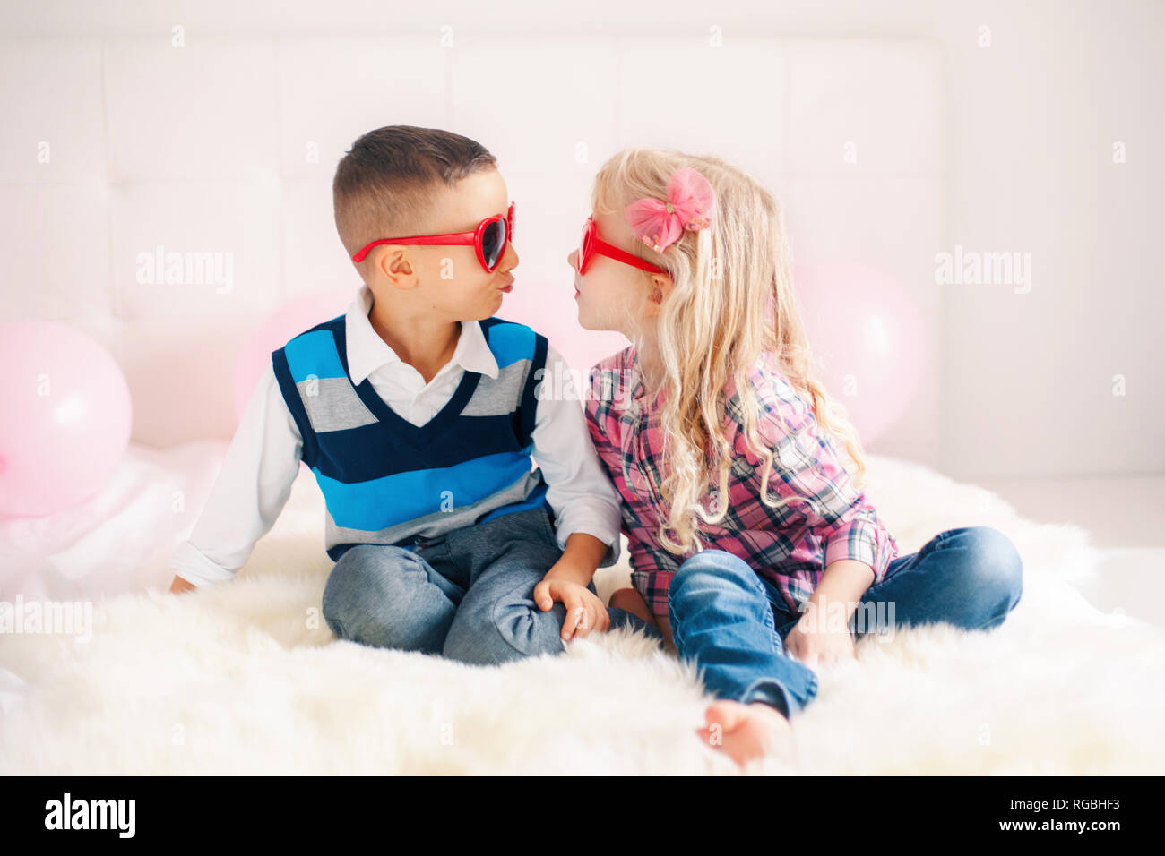 Portrait de deux professionnels white Caucasian mignon drôle adorables enfants portant des lunettes en forme de coeur. Garçon et fille essayant d'embrasser l'autre. L'amour, friendsh Banque D'Images