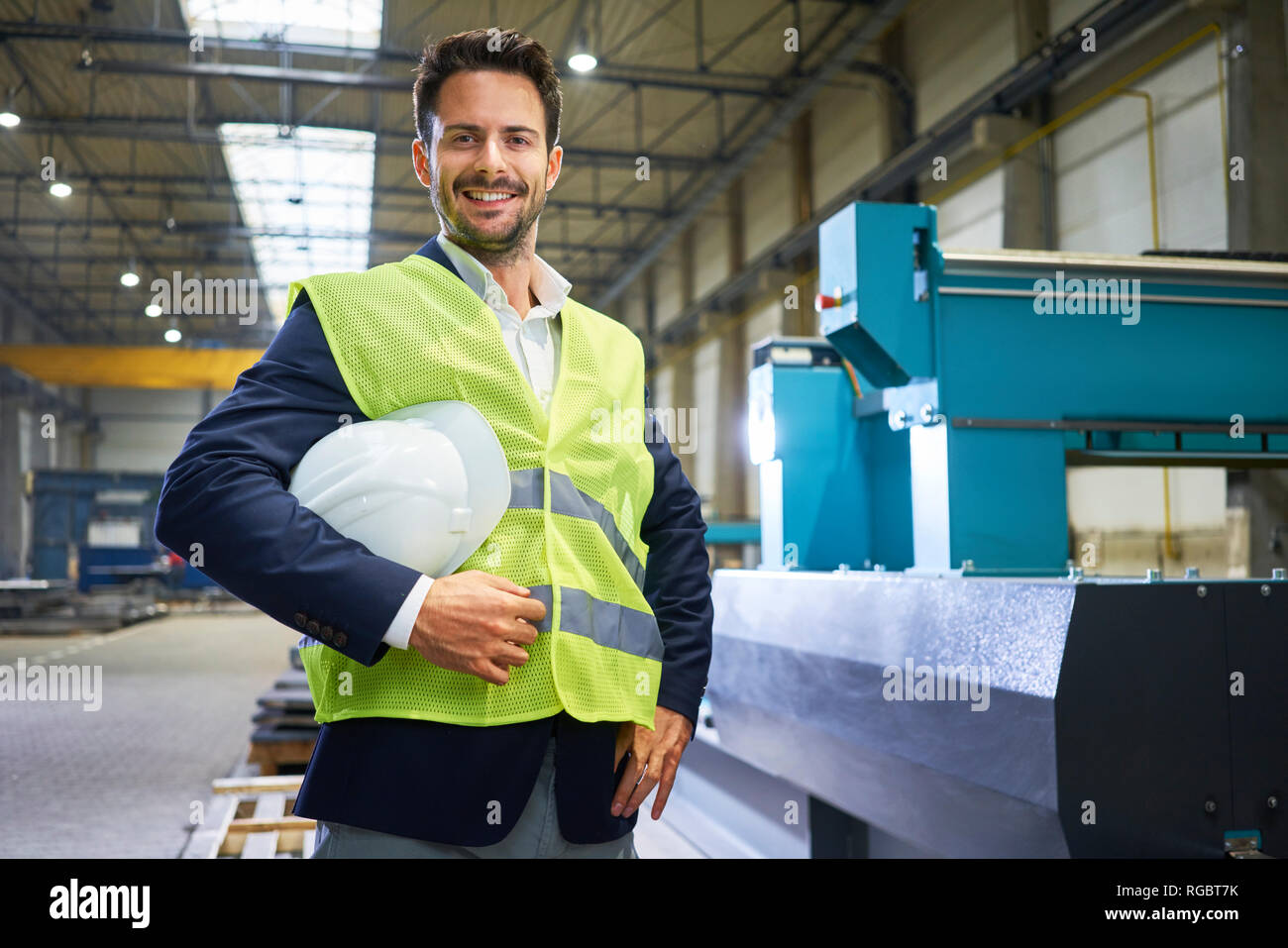 Portrait of smiling manager holding hard hat en usine Banque D'Images