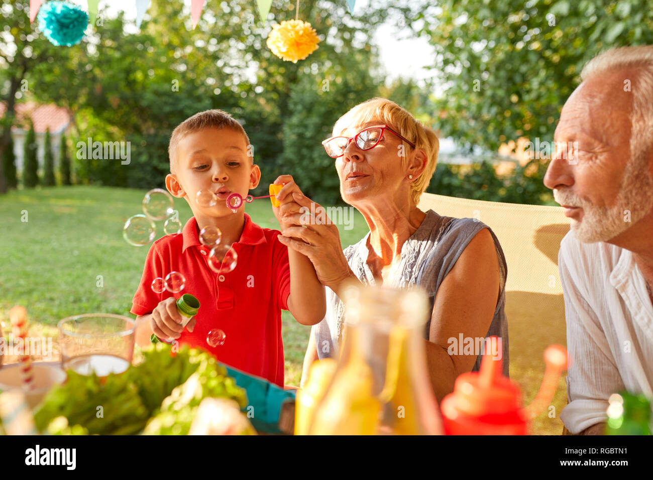 Grand-mère et petit-fils soufflant des bulles de savon on a garden party Banque D'Images