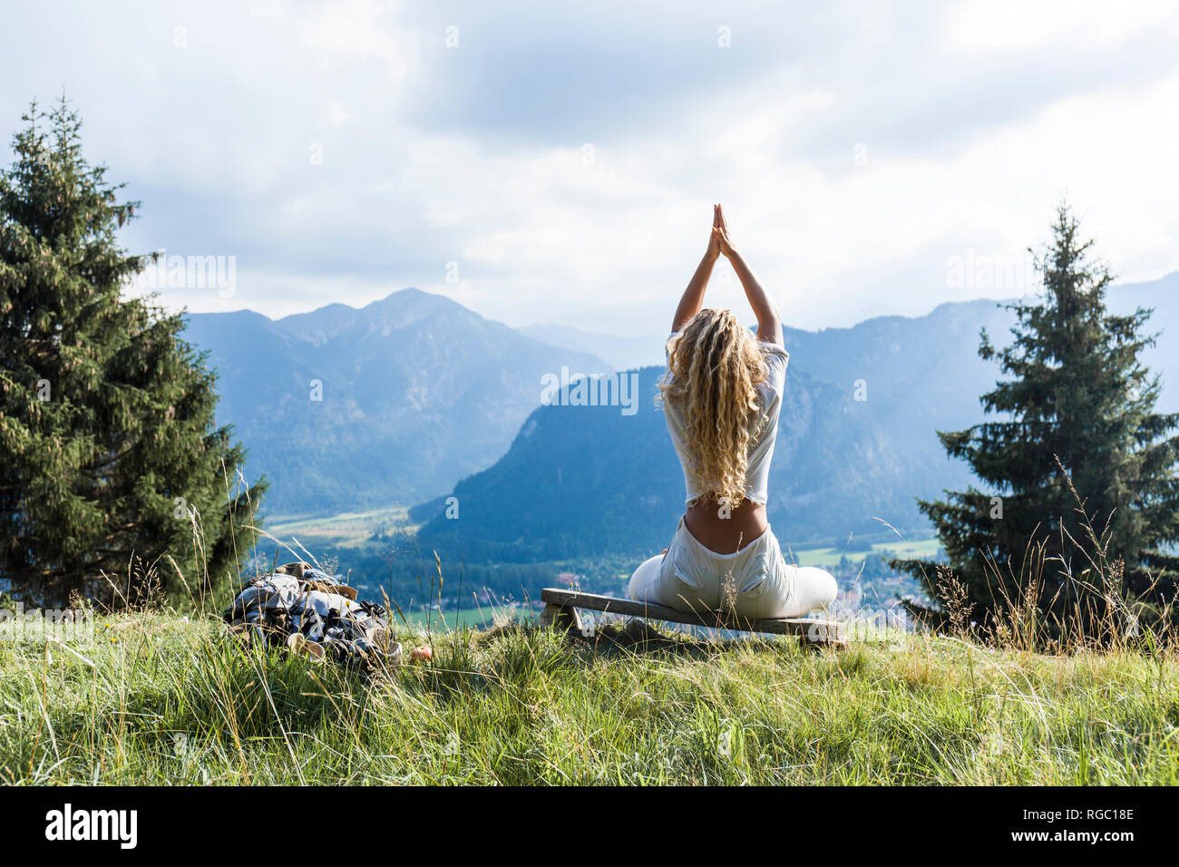 Germany, Bavaria, Oberammergau, young woman doing yoga sur banc mountain meadow Banque D'Images