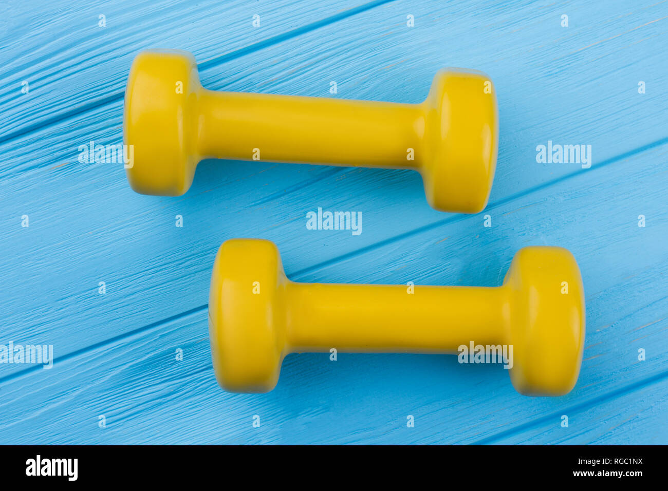 Haltères en bois jaune sur fond bleu. L'équipement de remise en forme sur des planches en couleur. Sport et mode de vie sain. Banque D'Images