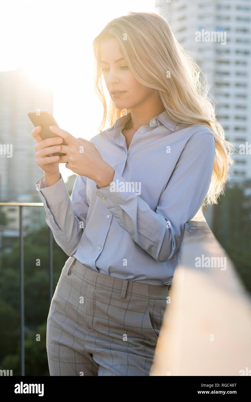 Femme d'affaires blonde contrôle du smartphone sur le toit de la ville Banque D'Images