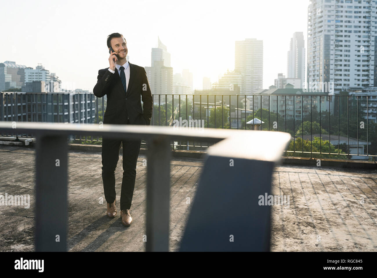 L'homme d'affaires en costume sombre en parlant du smartphone sur le toit de la ville Banque D'Images