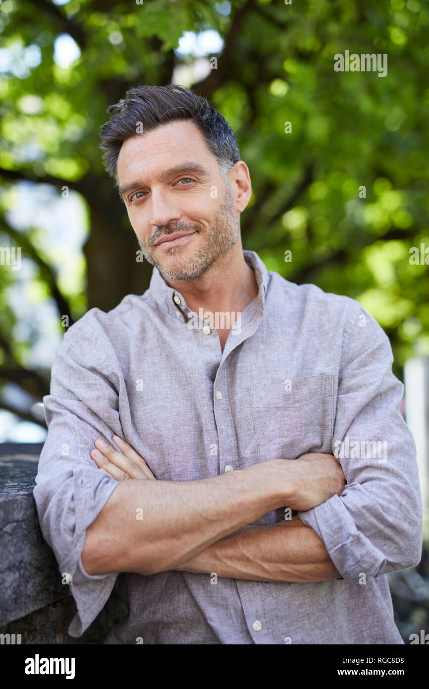 Portrait of smiling man with arms crossed leaning against wall Banque D'Images