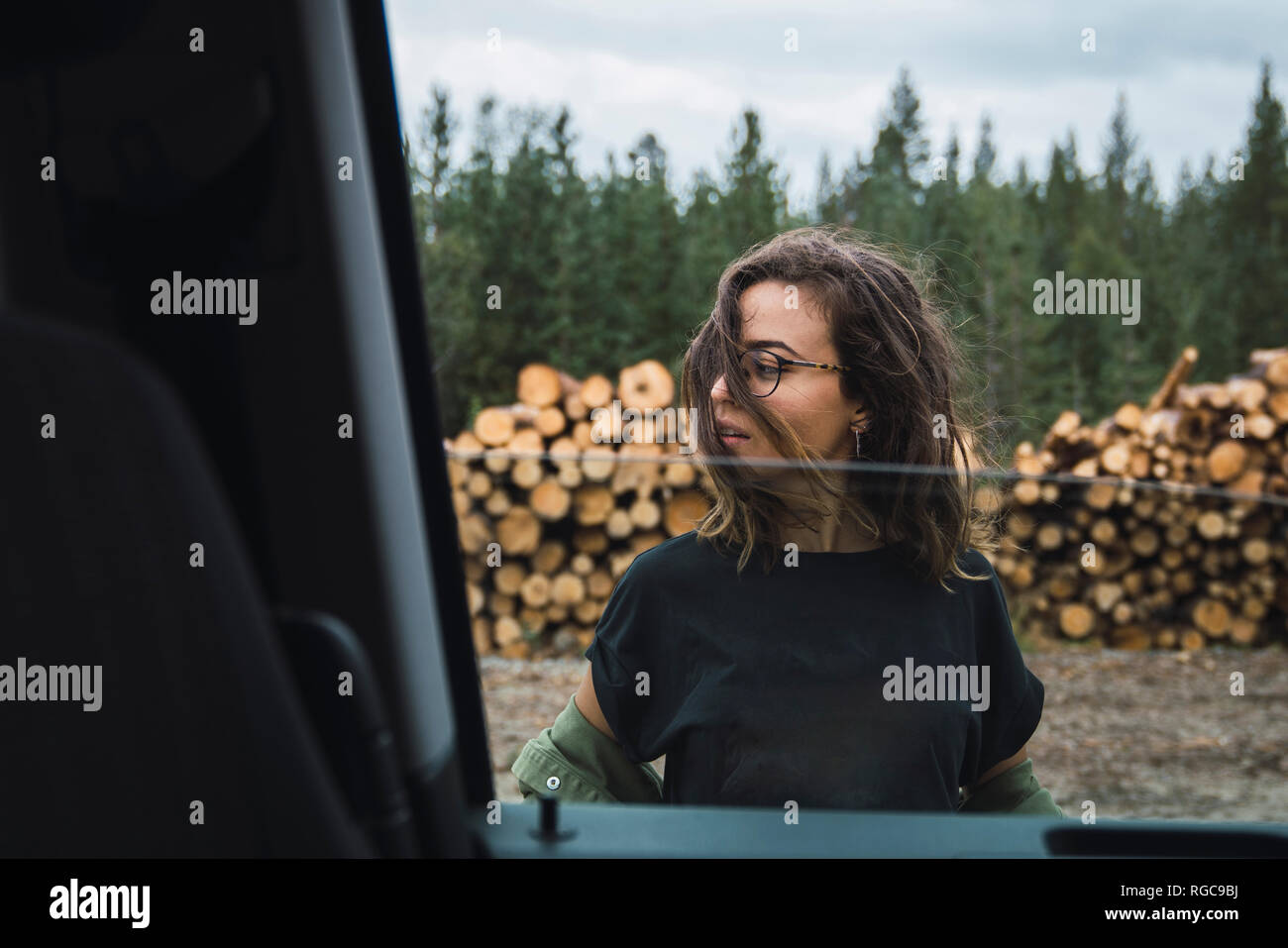 Jeune femme debout à côté de voiture à côté de la pile de bois Banque D'Images