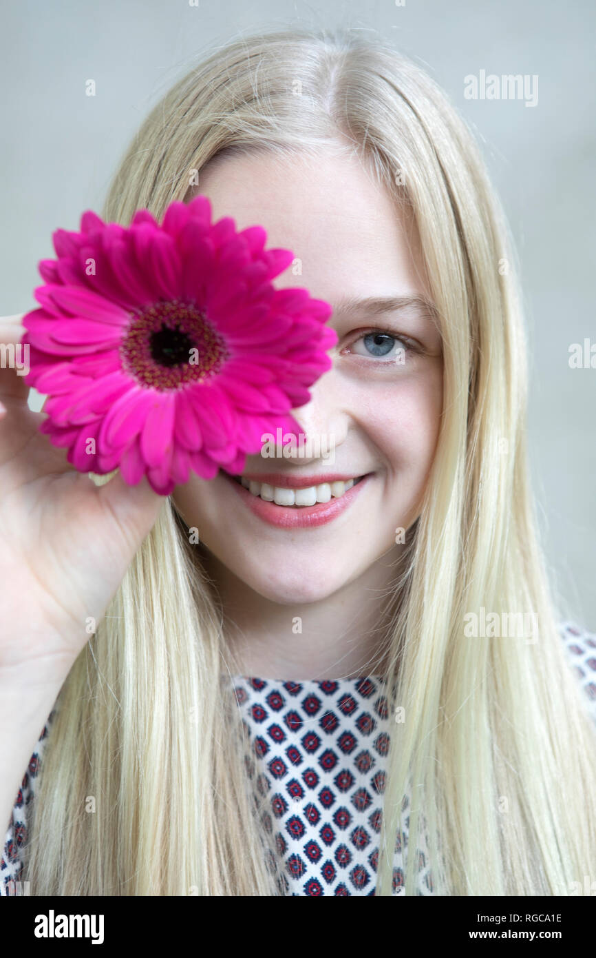 Portrait of smiling blonde avec fleur de Gerbera rose Banque D'Images