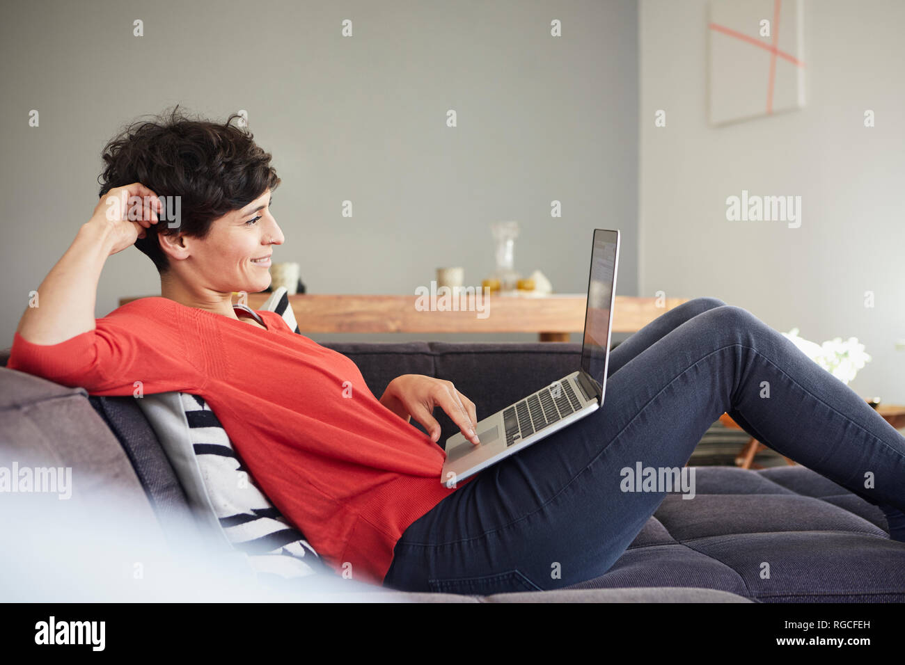 Smiling woman using laptop on couch at home Banque D'Images