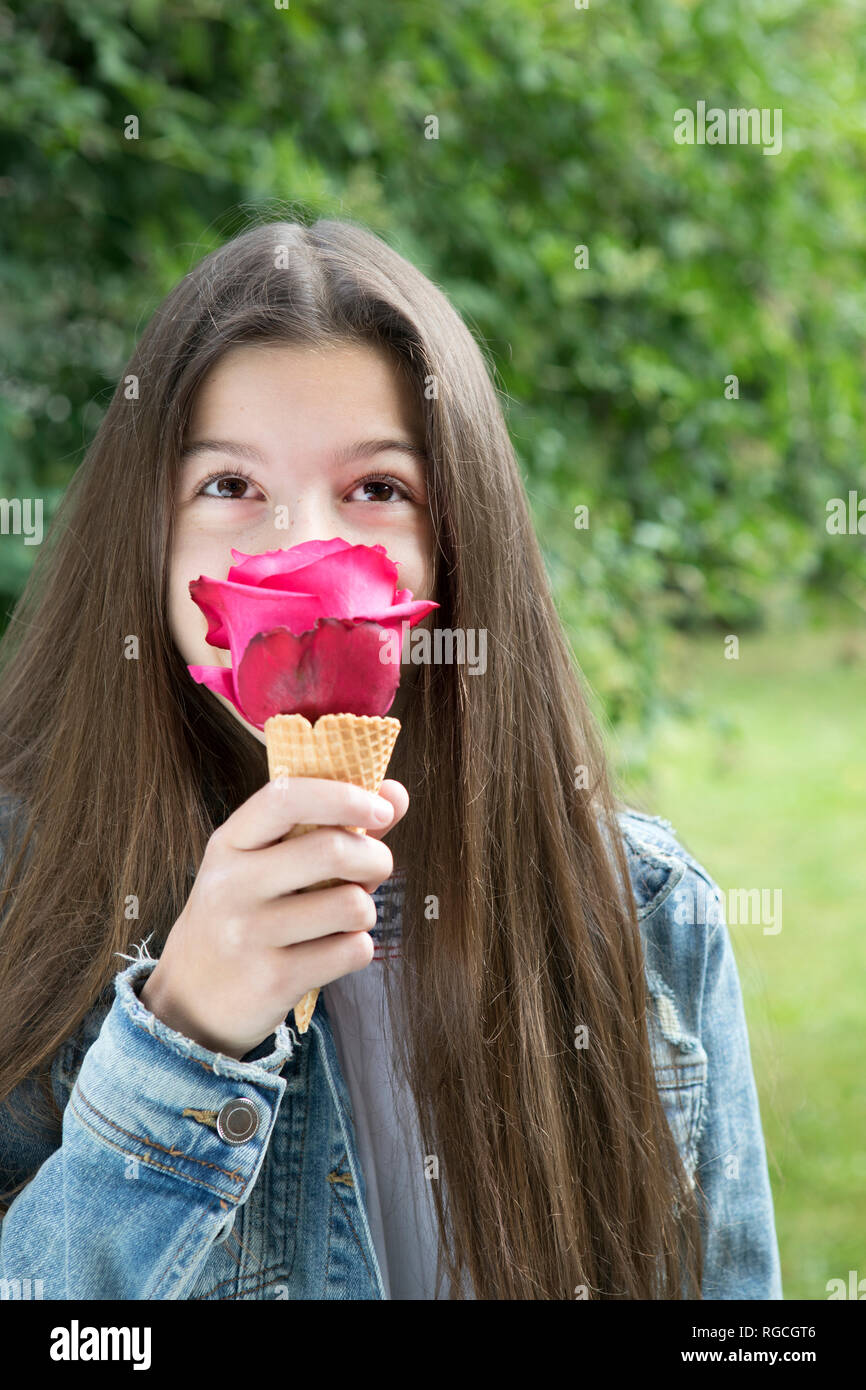 Girl smelling pink rose blossom dans ice cream cone Banque D'Images