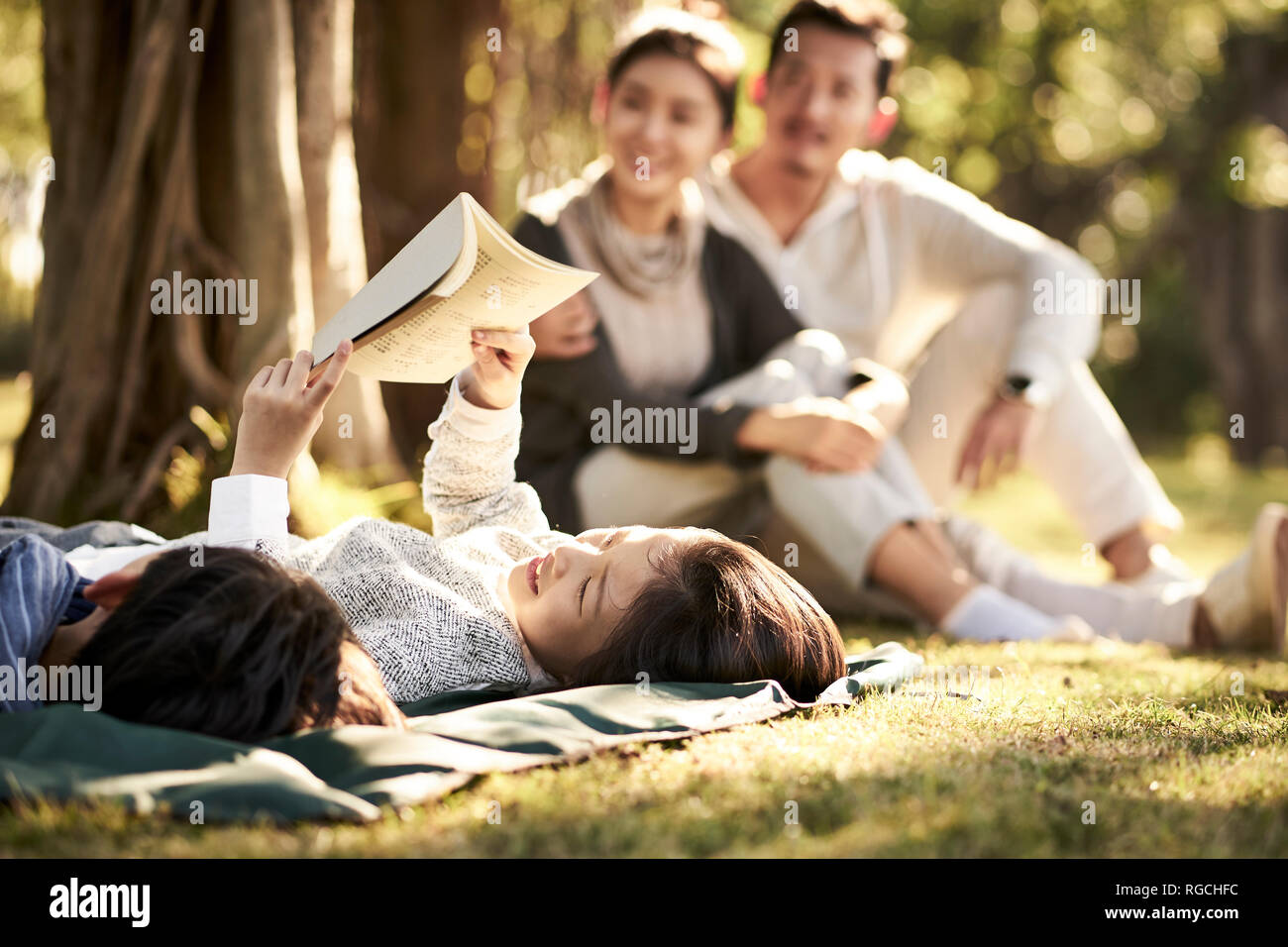 Deux enfants asiatiques little boy and girl having fun lying on grass avec les parents assis à regarder en arrière-plan, l'accent sur les enfants en premier plan. Banque D'Images