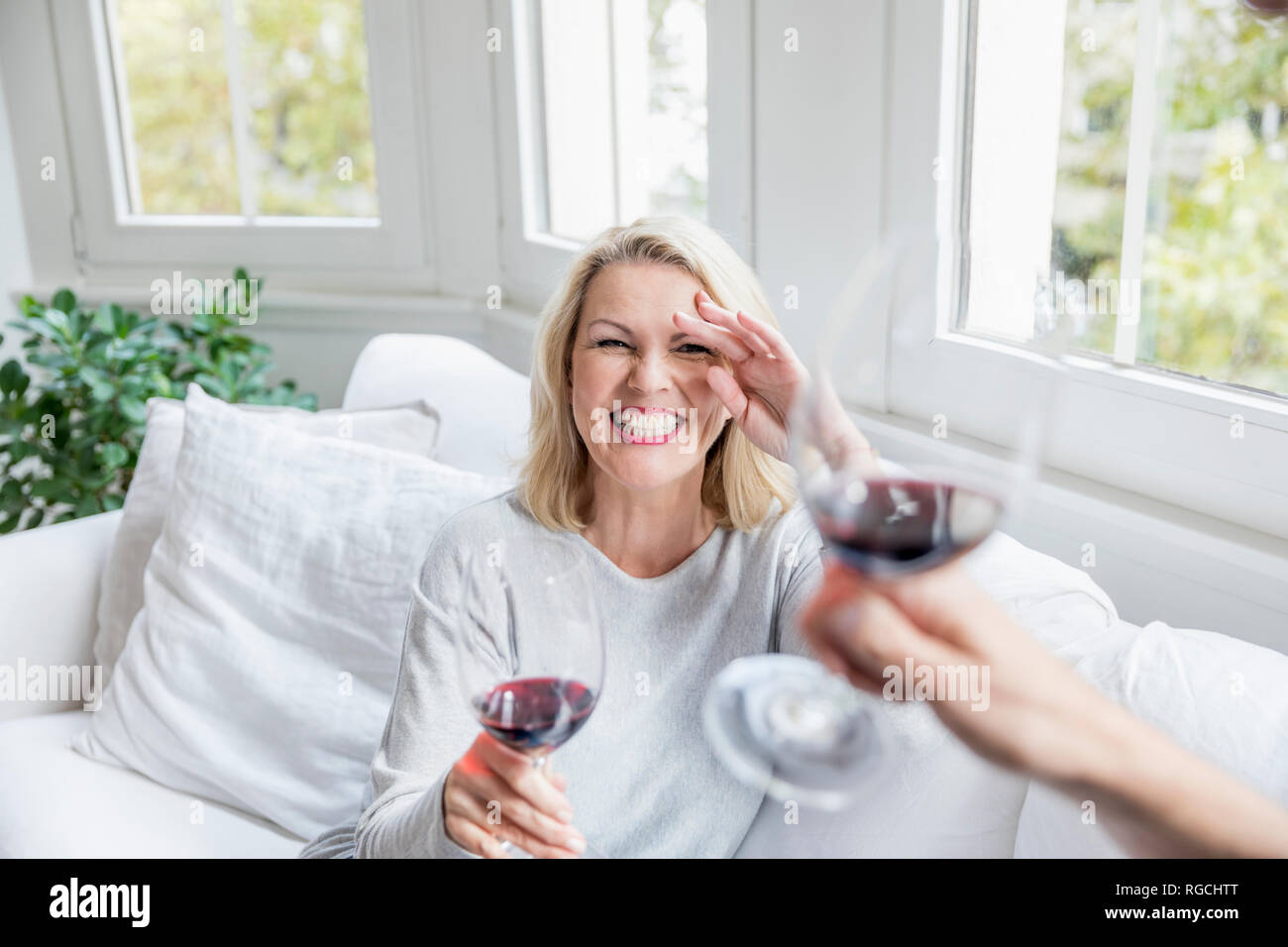 Portrait of laughing young blonde woman toasting avec du vin rouge à la maison Banque D'Images