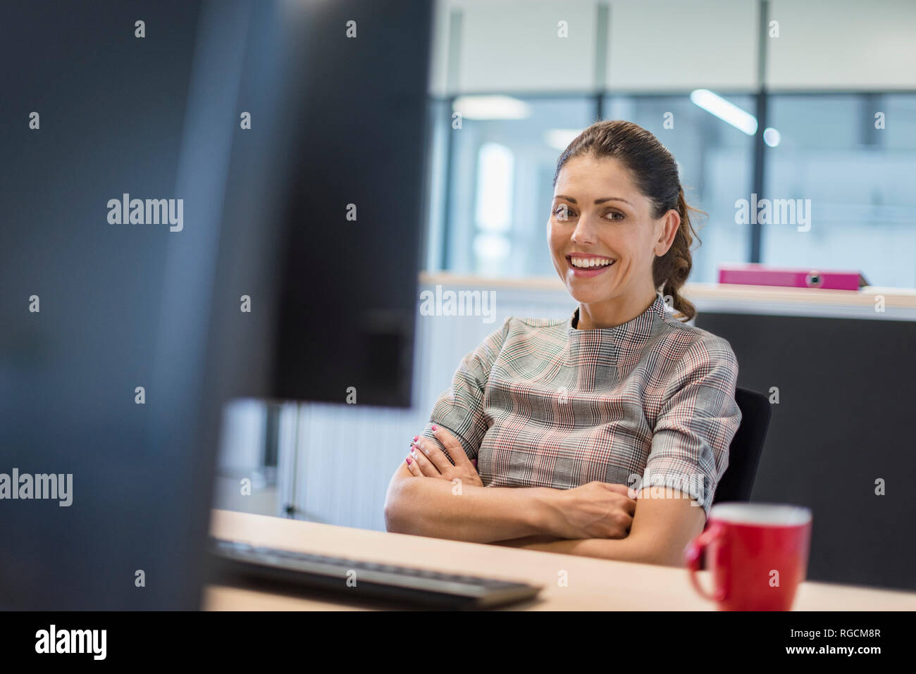Female office worker sitting at desk, avec les bras croisés Banque D'Images