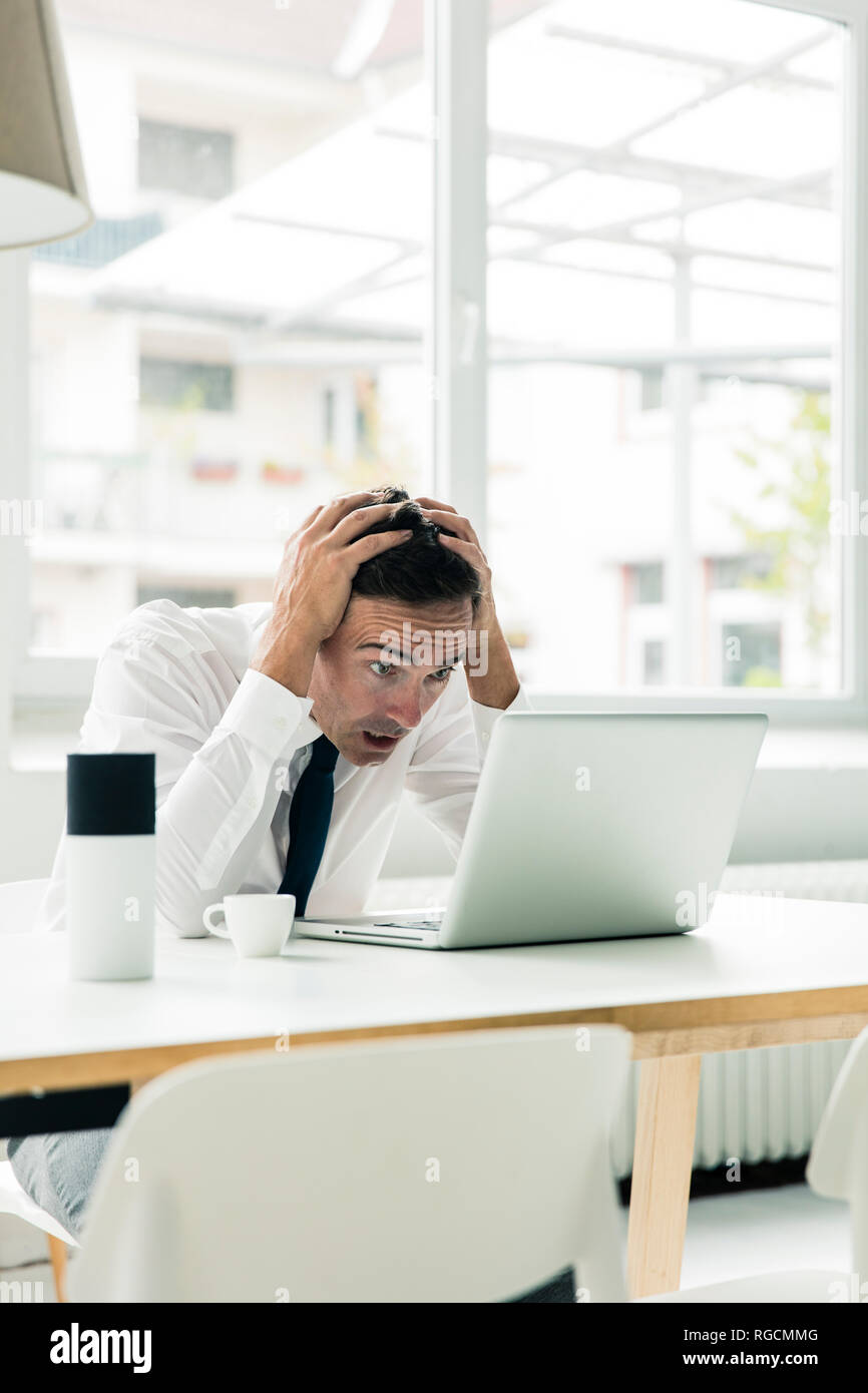 Choqué businessman looking at laptop on table in office Banque D'Images