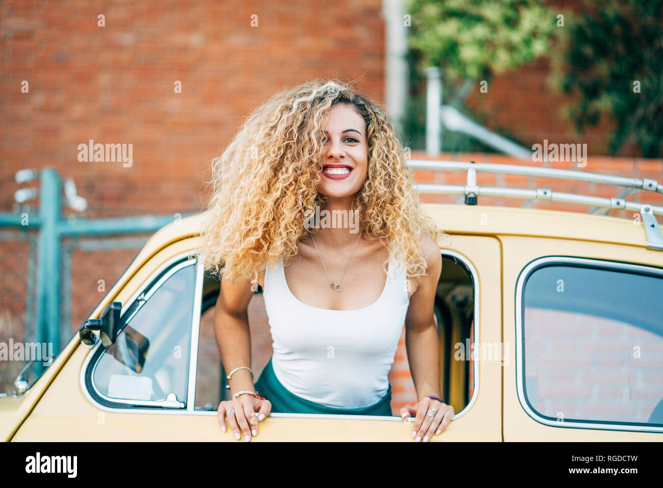 Portrait of happy blonde woman leaning out de la fenêtre de voiture classique Banque D'Images