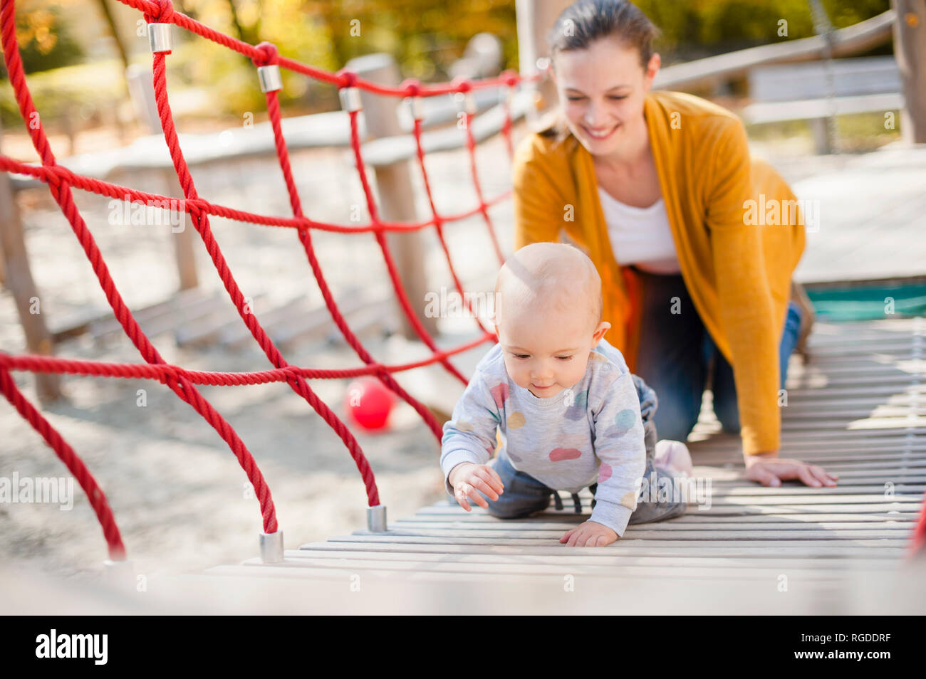Mère regardant son bébé fille jouant sur l'aire de jeux Banque D'Images Mère regardant son bébé fille jouant sur l'aire de jeux Banque D'Images