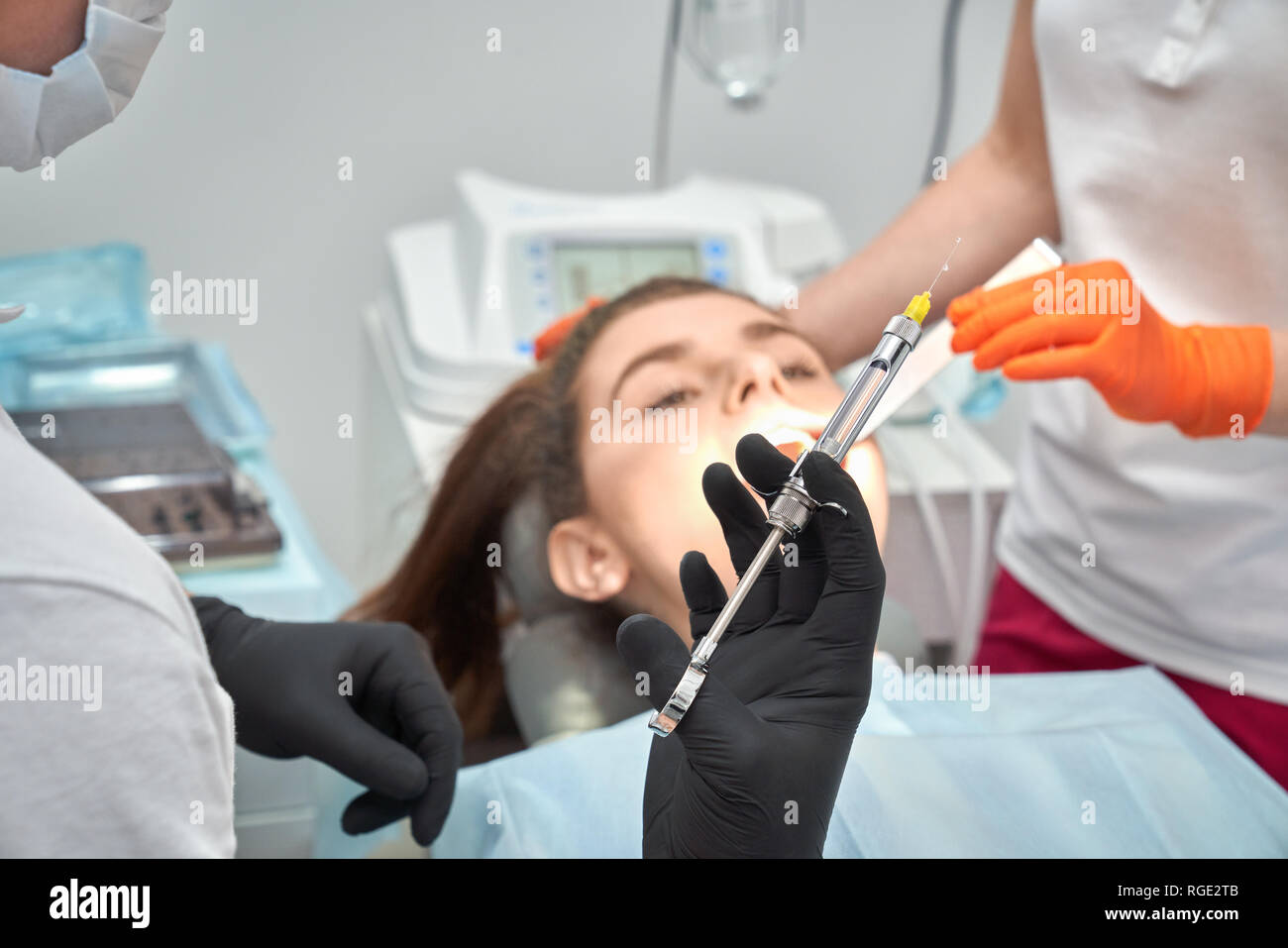 Dentiste dans les gants de maintien de la balle dans les mains et faire d'anesthésie et de client avant la procédure. Female patient lying on fauteuil dentaire à l'arrière-plan. Concept de prendre soin des dents et de traitement. Banque D'Images