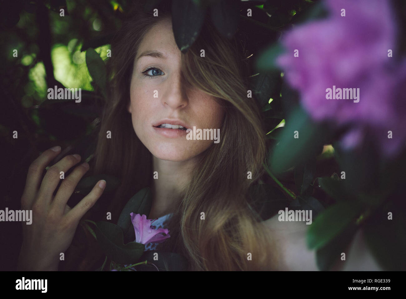 Belle jeune fille en robe blanche qui posent avec des fleurs, à la recherche dans l'appareil photo, un œil caché derrière ses cheveux Banque D'Images