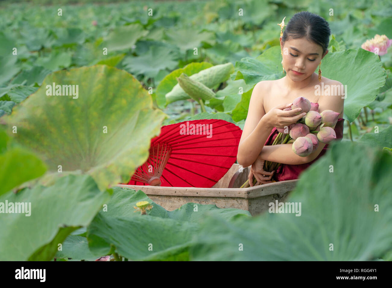 Belle Asie femmes portant robe traditionnelle thaïlandaise et assis sur le bateau en bois avec du papier rouge parapluie dans flower lotus lake. Elle a les mains tenant un p Banque D'Images