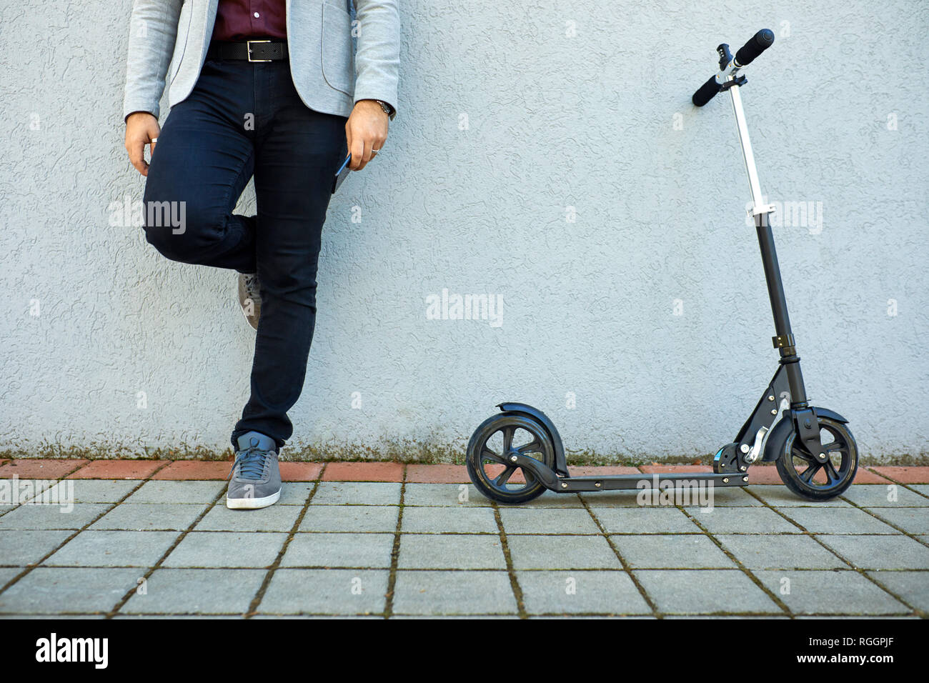 La section basse de businessman with scooter and cell phone appuyé contre un mur Banque D'Images