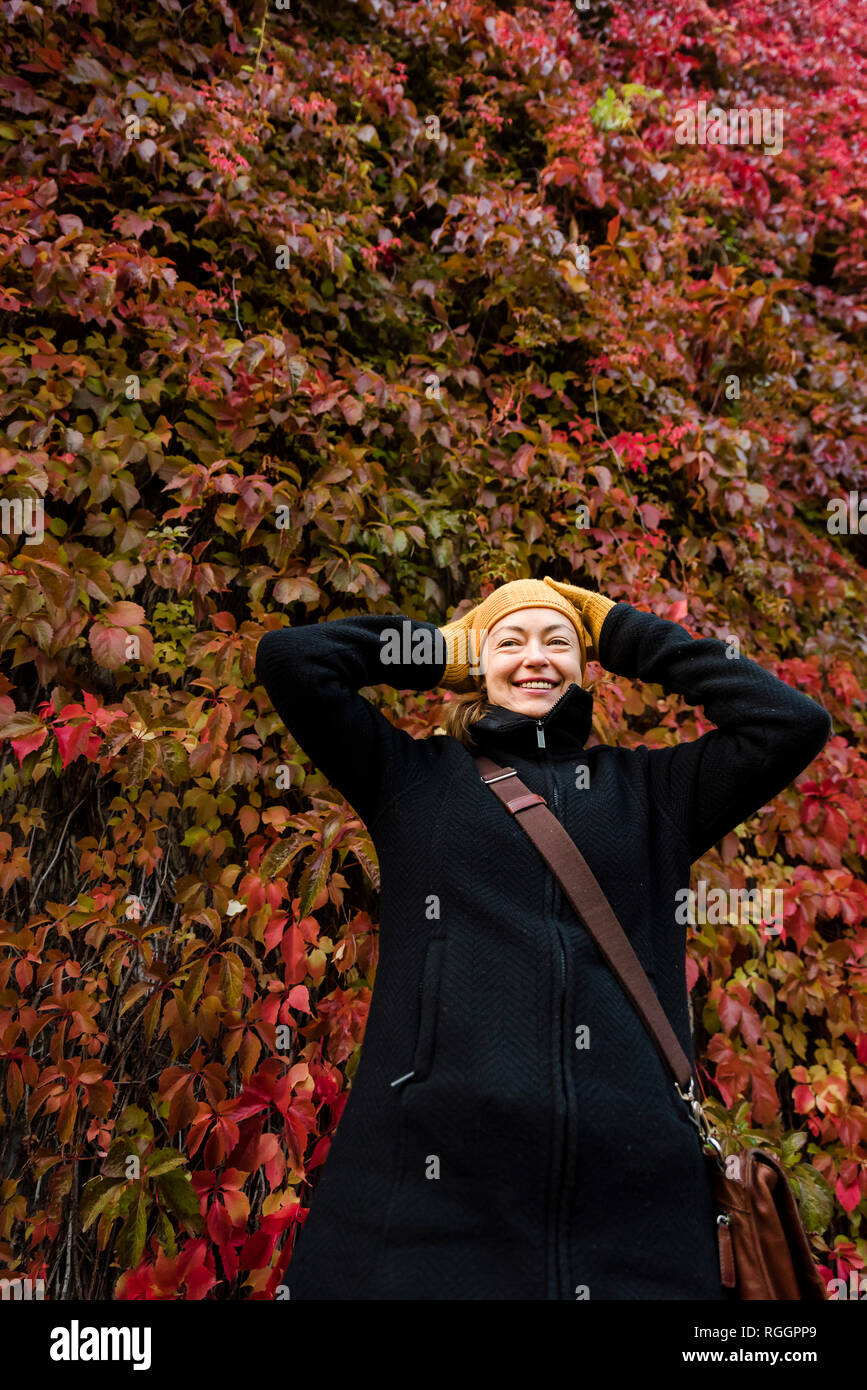 Portrait of smiling woman standing in front of wall envahie de vigne vierge en automne Banque D'Images