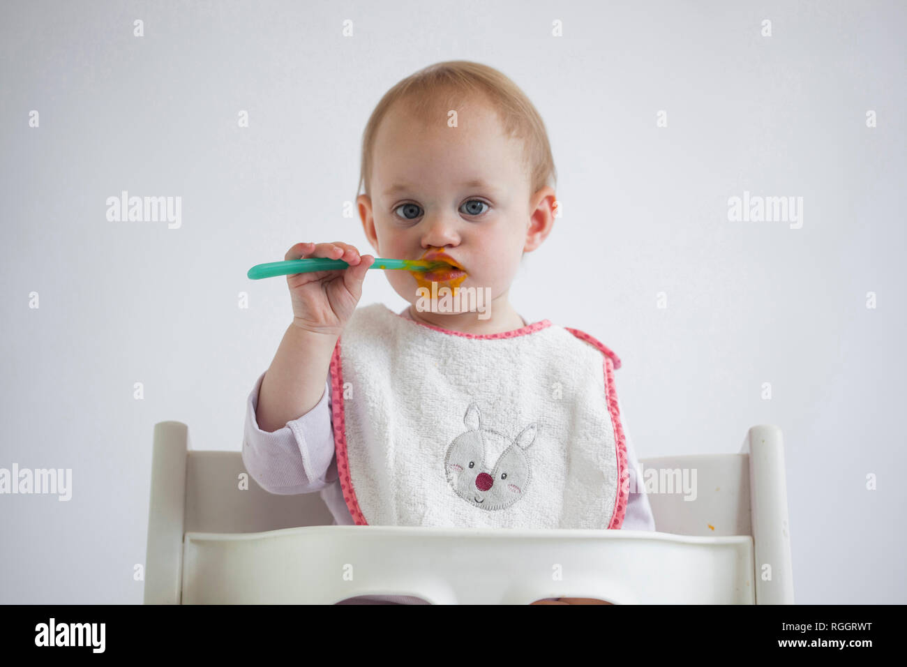 Portrait de jeune fille sur la chaise haute bébé manger bouillie Banque D'Images