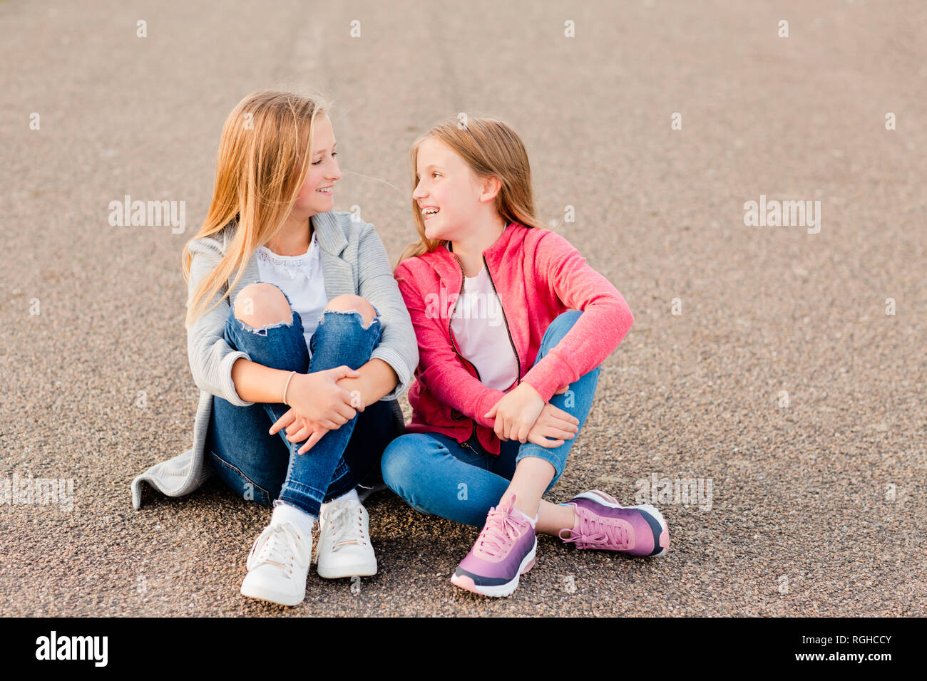 Deux filles souriant assis côte à côte sur le terrain Banque D'Images