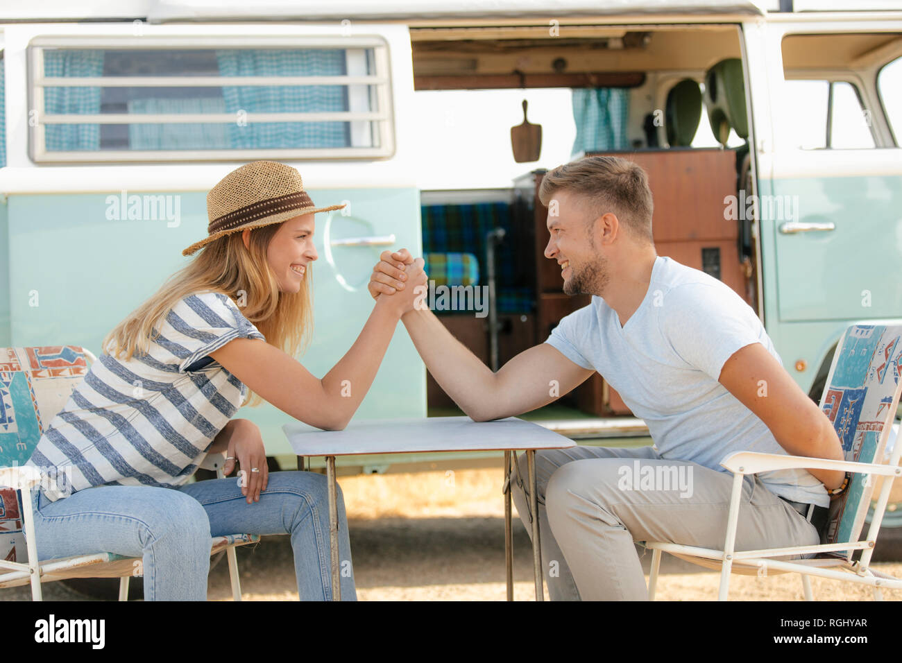 Happy young couple armwrestling sur chaises de camping en camping-van Banque D'Images