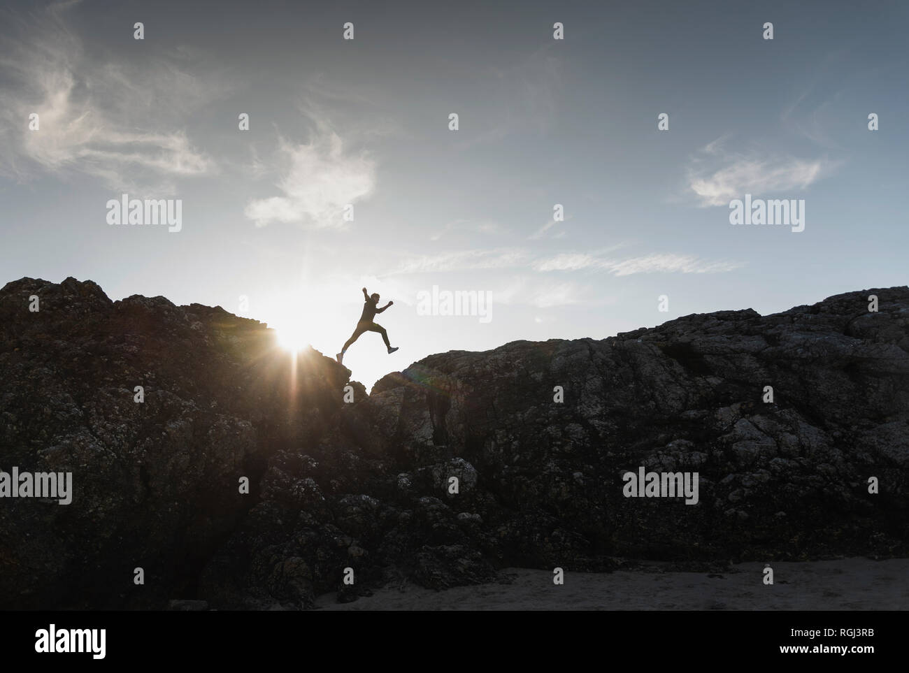 France, Bretagne, jeune homme sautant sur un rocher au coucher du soleil Banque D'Images