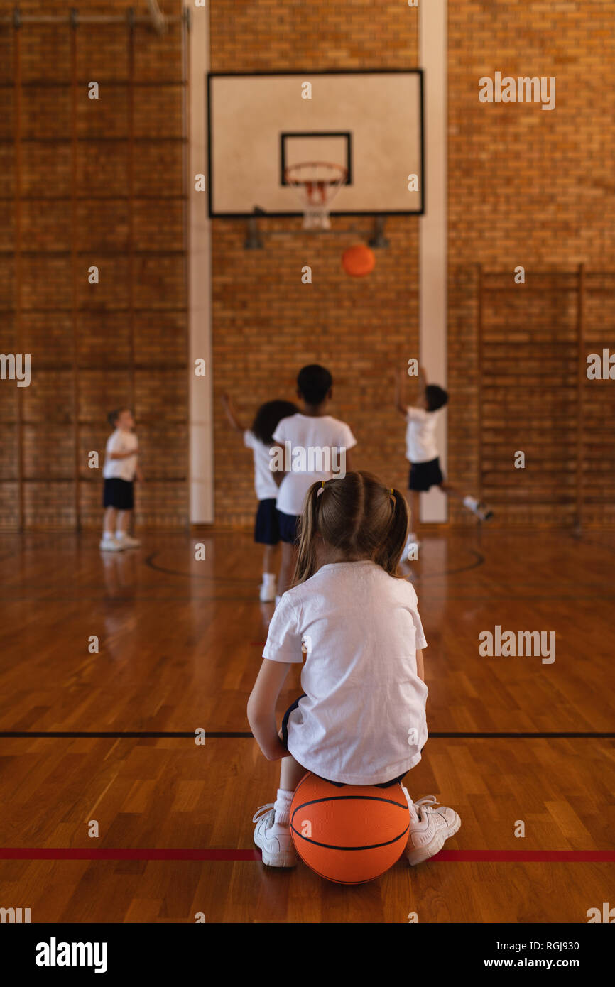 Vue arrière de lycéenne assis sur le basket-ball au basket-ball Banque D'Images