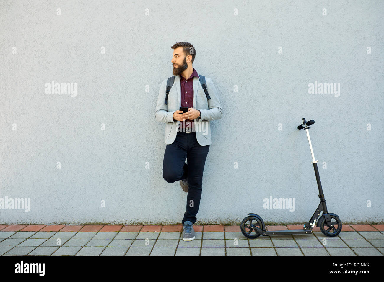 Businessman with scooter and cell phone appuyé contre un mur Banque D'Images