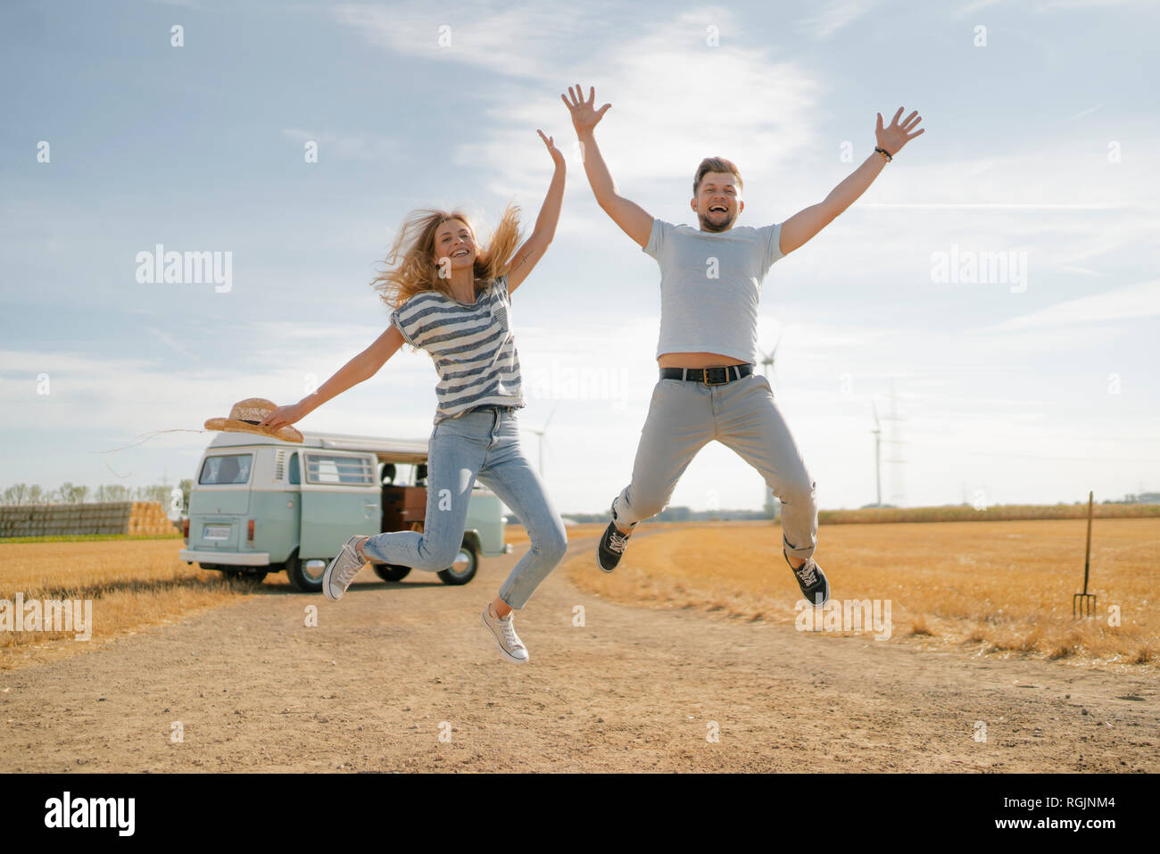 Couple exubérant de sauter sur un chemin de terre à camper van in rural landscape Banque D'Images